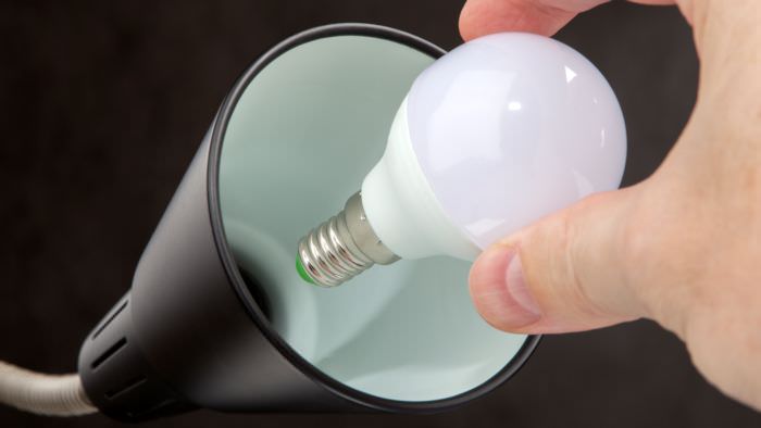 Person Screwing Lightbulb Into Lamp